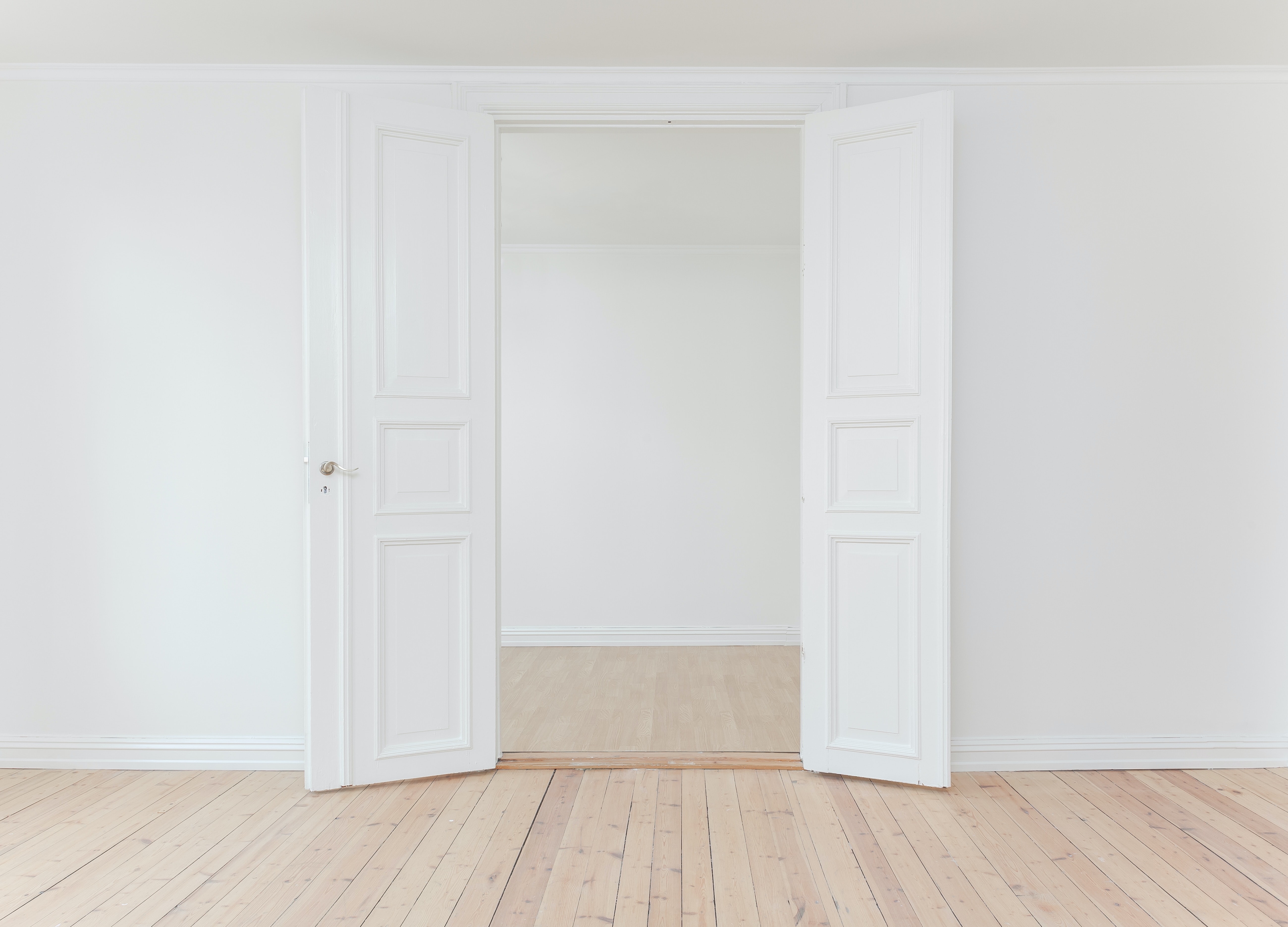 A photo of a bright, wooden-floored interior entrance with tall, white, decorated double doors